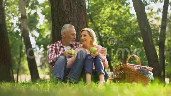 家庭周末退休夫妇坐在公园里吃绿苹果野餐视频的预览图