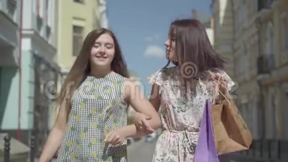两个快乐的女人带着购物袋穿过城市街道年轻女孩穿着时髦的夏装视频的预览图