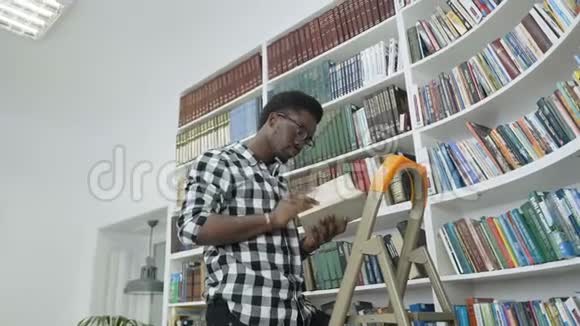 非洲男学生在大学图书馆里站在梯子上从书架上看书视频的预览图