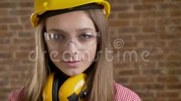 年轻迷人的女建筑工人触摸头盔笑着看镜头砖背景视频的预览图