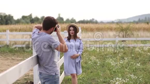 摄影师为穿着蓝色连衣裙和针织帽子的美丽孕妇制作照片她把手放在视频的预览图