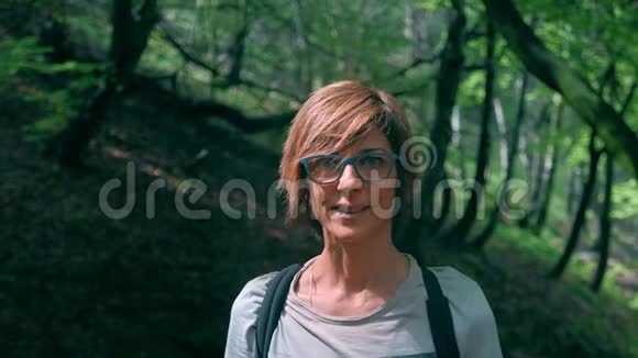 森林里户外的成年妇女肖像微笑着看着相机戴着绿色眼镜表情开朗h视频的预览图