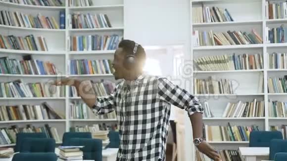 快乐的非洲年轻人在耳机里听音乐在图书馆里跳舞视频的预览图