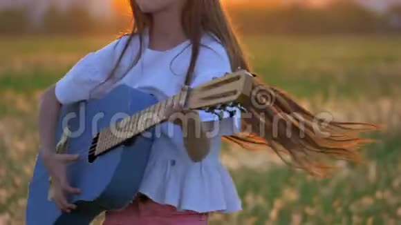 在日落时分有趣的小女孩在蒲公英地弹吉他远离城市建筑的户外情感和乐趣视频的预览图