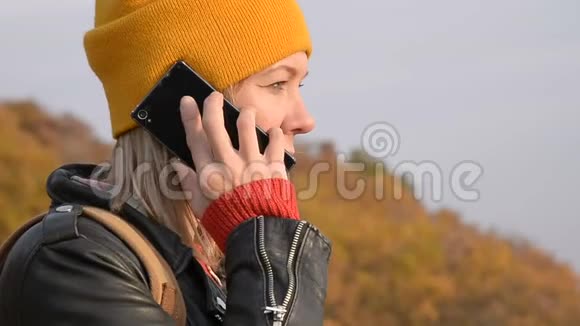 秋天一个戴着黄色帽子的漂亮白种人女孩正在户外用手机聊天微笑的女孩视频的预览图