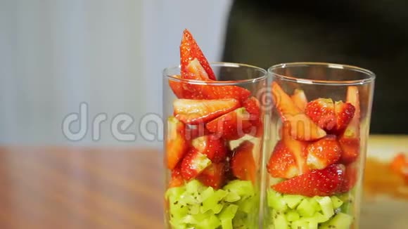 一个女人把碎奇异果片和成熟的草莓放进杯子里视频的预览图