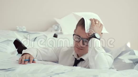 一个戴眼镜的疲惫的年轻人坐在一堆文件和签名文件里他把头捏在手心里视频的预览图