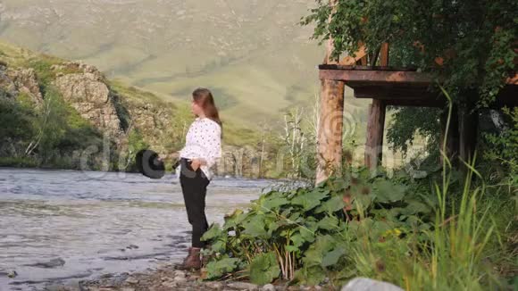漂亮的深色头发戴着帽子穿着白衬衫穿着豌豆在山上享受着大自然年轻的女游客散步视频的预览图
