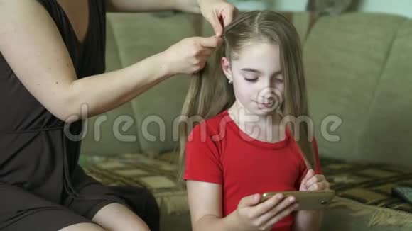 女人她的手为她的小女儿做发型一个女人正在为她的女儿编织头发视频的预览图