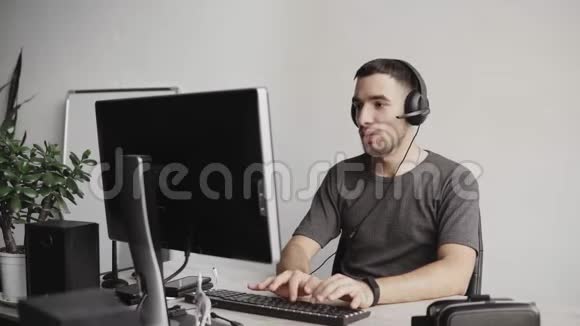 年轻的商人或穿着衬衫的学生坐在耳机和电脑显示器旁视频的预览图