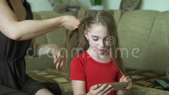 女人她的手为她的小女儿做发型一个女人正在为她的女儿编织头发视频的预览图