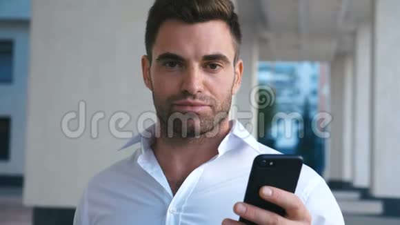 年轻有魅力的商人在办公楼附近使用智能手机看上去很成功戴着长胡子的帅哥视频的预览图