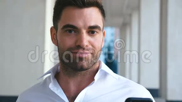 年轻的成功商人在办公大楼附近使用智能手机穿白色衬衫的长胡子帅哥商务视频的预览图