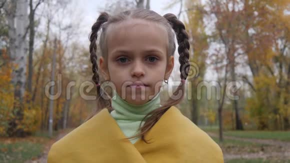 特写一个小女孩在镜头前微笑的肖像女孩在公园里穿黄色外套视频的预览图