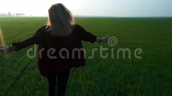 日落时分年轻美丽的金发少女在一片新鲜的绿色麦田上奔跑穿着一件格子红衬衫穿过田野视频的预览图