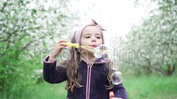小女孩在盛开的花园里玩肥皂泡慢动作视频的预览图