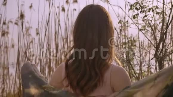 年轻的姜黄色微笑的女孩穿着一件连衣裙站在大自然的树林里远远地看着相机50fps视频的预览图