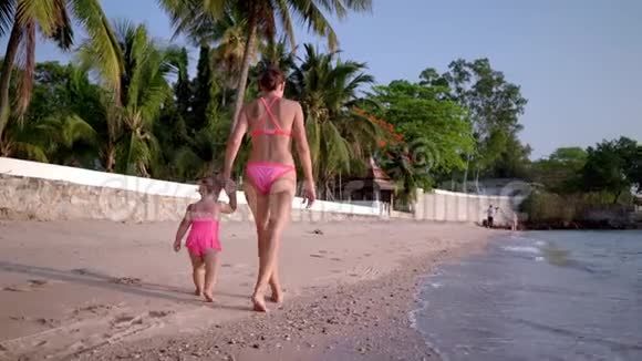 妈妈和小女儿穿着粉色泳衣沿着海滨散步后景慢动作视频的预览图