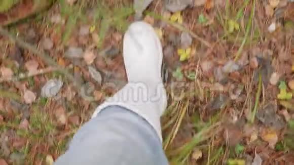 穿着白色口香糖靴子在秋天森林里散步的人的腿视频的预览图