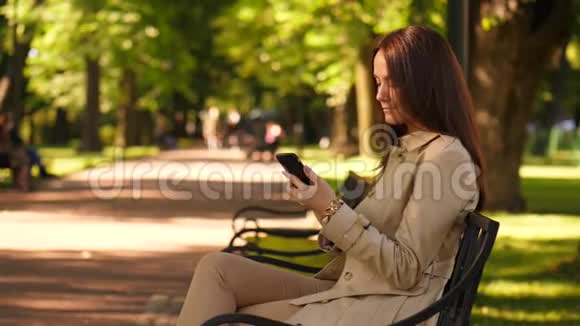 女人用智能手机坐在公园里视频的预览图
