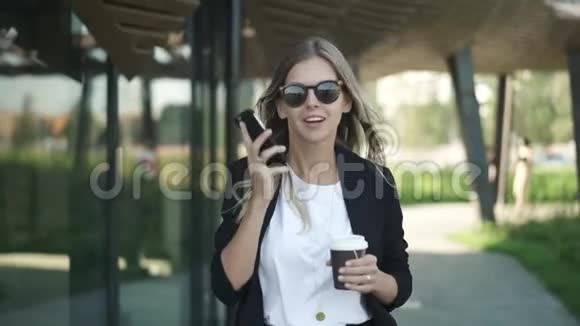 戴墨镜的金发女人带着咖啡和智能手机聊天视频的预览图