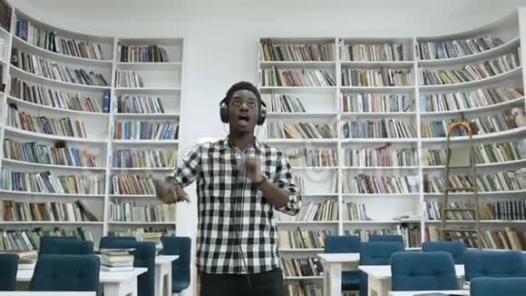 年轻的非洲男学生在现代图书馆里跳舞在耳机里听音乐视频的预览图