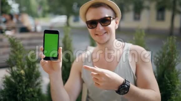 旅行者手拿着带有绿色屏幕的智能手机的肖像看着相机微笑着视频的预览图