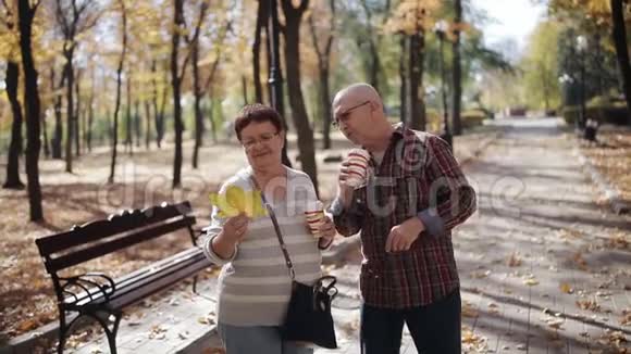 一对老夫妇在秋天公园散步一个年老的男人和女人在公园散步喝着咖啡说话视频的预览图