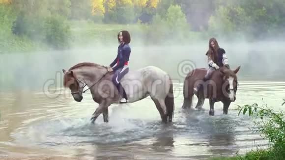 两个骑马的年轻女子站在湖里马蹄声在夕阳下清晨泼水全都是视频的预览图