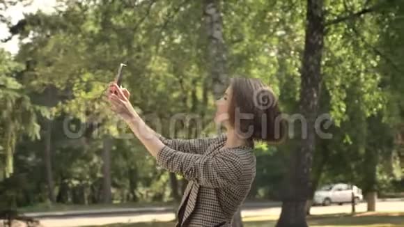 年轻迷人的女孩白天在公园里自拍鸭脸夏天交流理念侧视视频的预览图