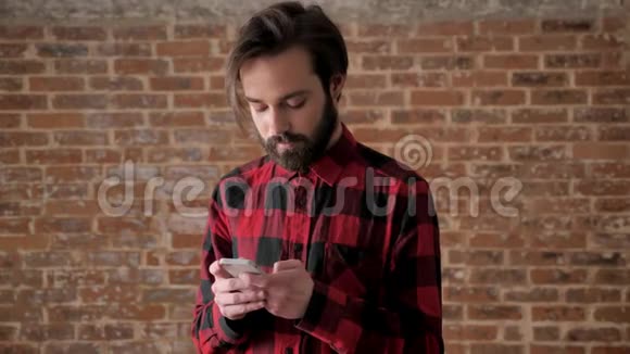 年轻的帅哥在他的智能手机上有胡须类型的信息通信概念砖背景视频的预览图