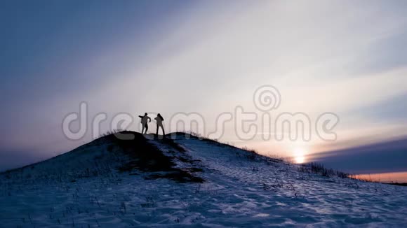 登山者两个背着背包的旅行者的剪影向对方展示了冬季登山时的相机视频的预览图