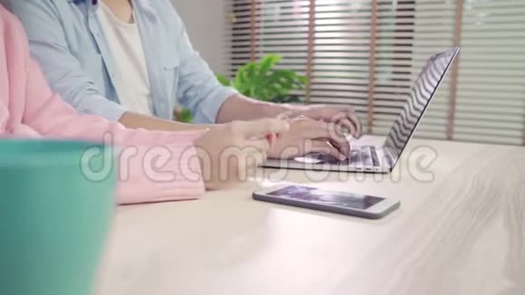 年轻的亚洲家庭夫妇使用笔记本电脑讨论新闻或做网上购物一起坐在办公桌上周末在家里视频的预览图