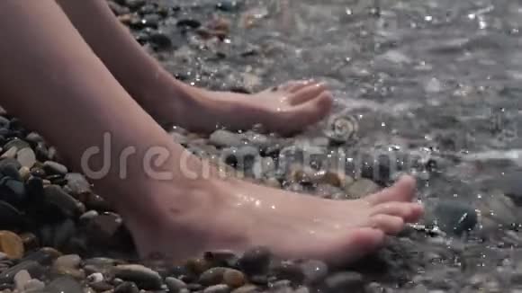 一个孩子的腿特写被波浪淹没了卵石沙滩喧闹的海浪拍打着孩子们双腿视频的预览图