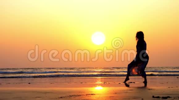 年轻体操女子在日落时在沙滩上做手弹簧的剪影视频的预览图