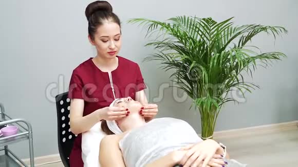美容师在水疗沙龙为年轻女性做放松的面部按摩视频的预览图
