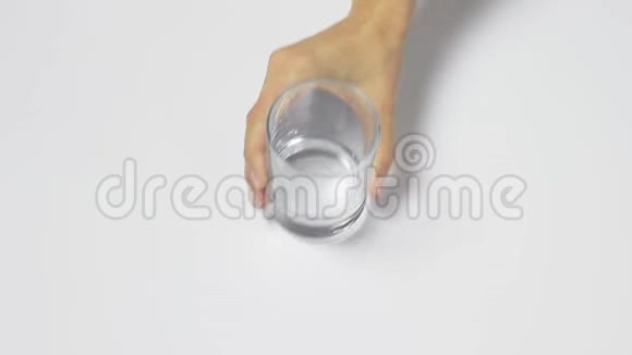 女人手把一个透明的空玻璃放在白色的桌子上往里面倒纯净水然后把拿下来视频的预览图