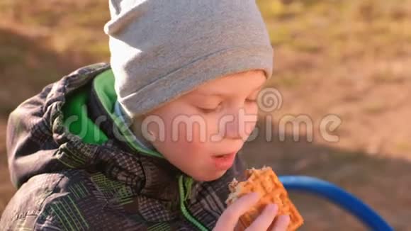 男孩坐在公园的长凳上吃华夫饼特写的脸视频的预览图