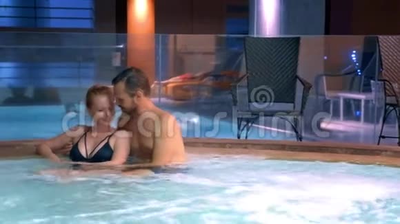 情侣们在室外热水浴缸中放松快乐的年轻女人和男人在游泳池附近的热水中放松视频的预览图