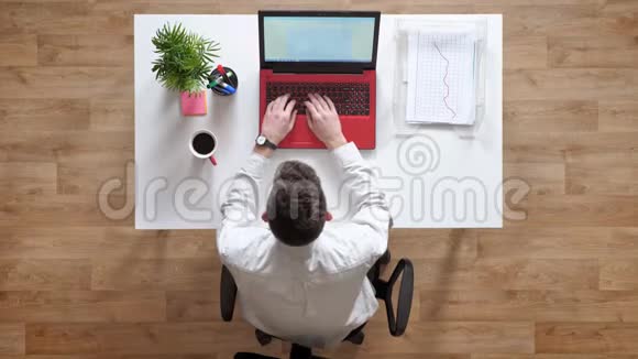 年轻人在笔记本电脑上打字看着显示器上面的镜头坐在桌子后面拿着文件和咖啡视频的预览图