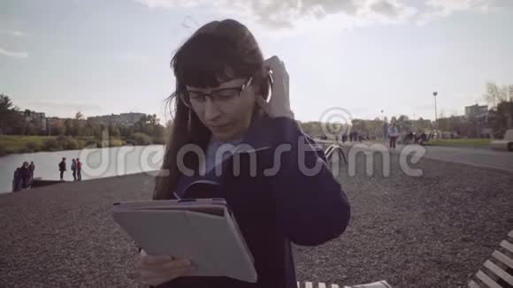 戴眼镜的商务女士在河岸用米黄色的平板电脑视频的预览图