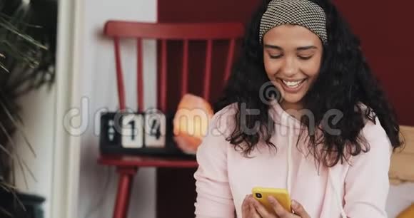 漂亮的年轻女人一边微笑一边在黄色的智能手机上聊天坐在家里的床上女孩向视频的预览图
