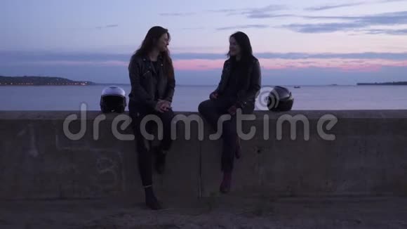两个年轻的女孩骑自行车坐在海边在堤岸放松视频的预览图
