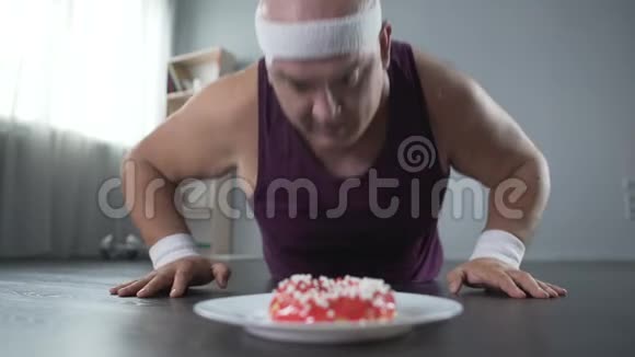 穿着运动服的胖子做俯卧撑看着面前美味的甜甜圈视频的预览图