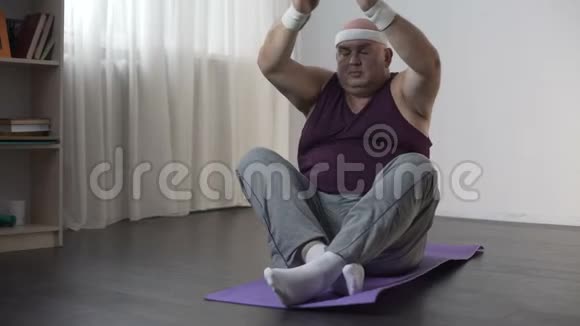 肥胖的男人坐在垫子上摔倒在地有趣的胖乎乎的男人在做瑜伽视频的预览图