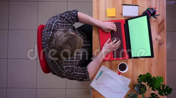 一位年轻的高加索商人在办公室里用带咖啡的绿色屏幕制作笔记本电脑的特写镜头视频的预览图