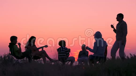 日落时分人们坐在海滩上篝火旁视频的预览图