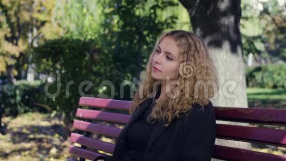 秋天多姿的公园里美女坐在树旁的长凳上视频的预览图