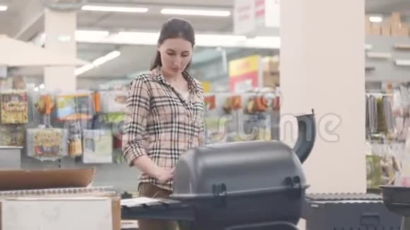 一个穿格子衬衫的女孩在商店里看烤架的画像视频的预览图
