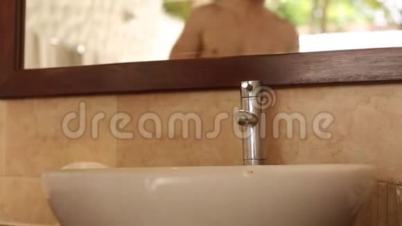 在热带岛屿的平房浴室里男人在镜子前刮胡子视频的预览图